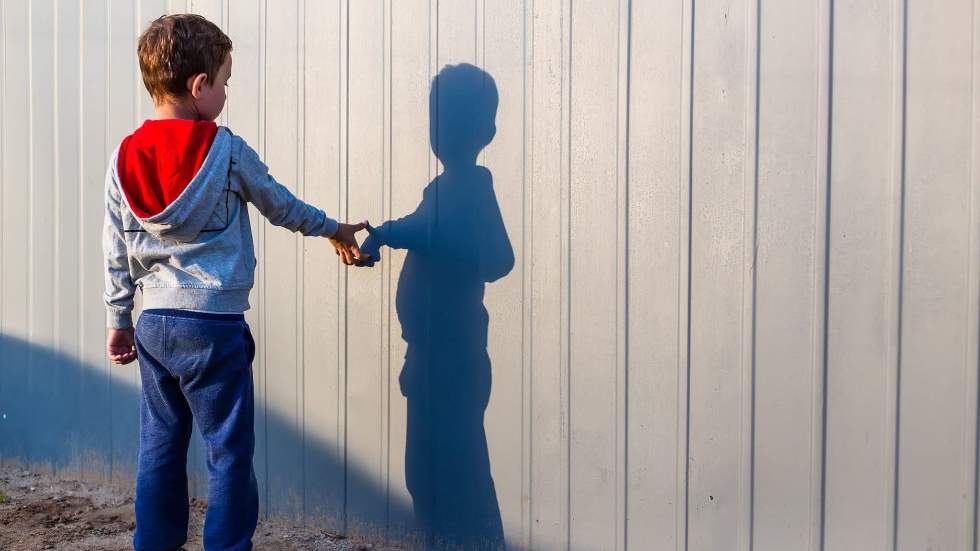 Un enfant touche la main de son ombre projetée sur une palissade comme s'il touchait la main d'un ami