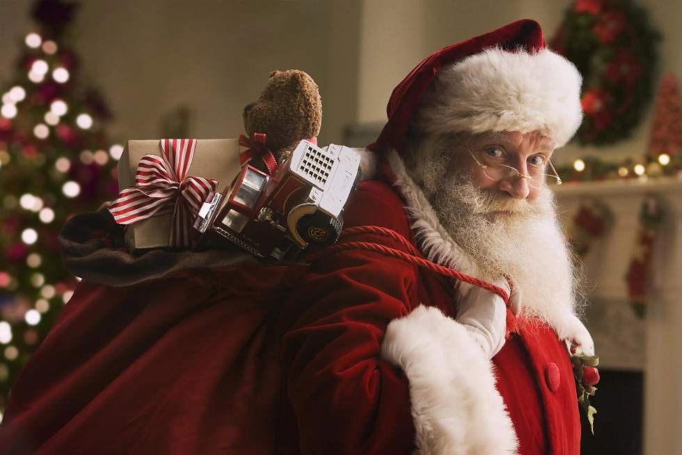 Un homme déguisé en Père Noël et avec un sac rempli de cadeaux nous regarde